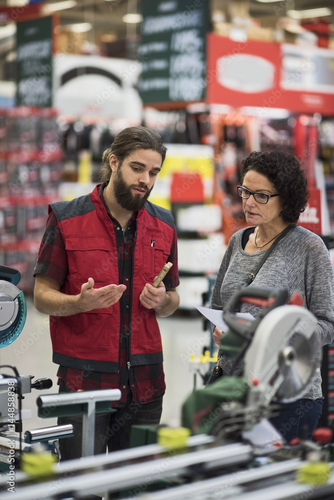 Salesman explaining power tools to mature woman in hardware store Salesman explaining power tools to mature woman in hardware store