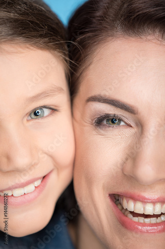 headshot portrait of happy mother and daughter hugging in studio on blue
