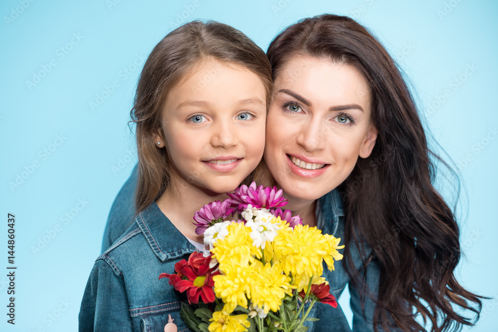 happy mother and daughter hugging and holding flowers in studio on blue, Happy mothers day happy mother and daughter hugging and holding flowers in studio on blue, Happy mothers day