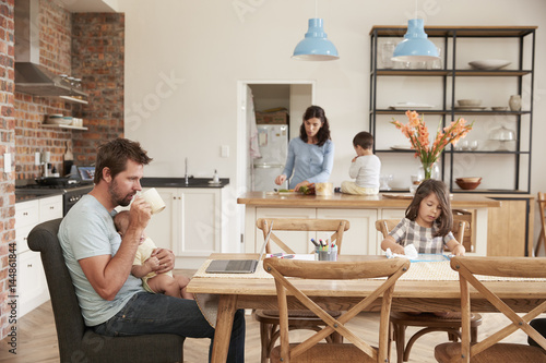 Busy Family Home With Father Working As Mother Prepares Meal