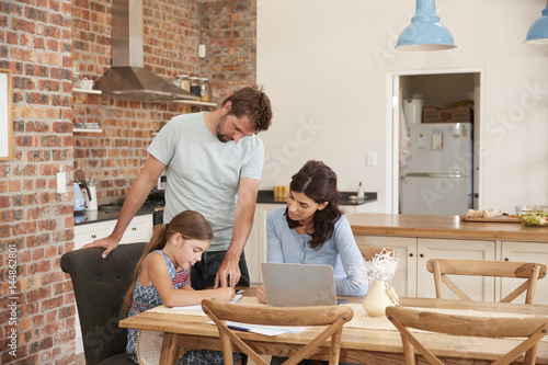 Parents Helping Daughter With Homework At Kitchen Table