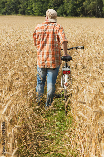Traveller in cap and sunglasses with a bicycle at the field