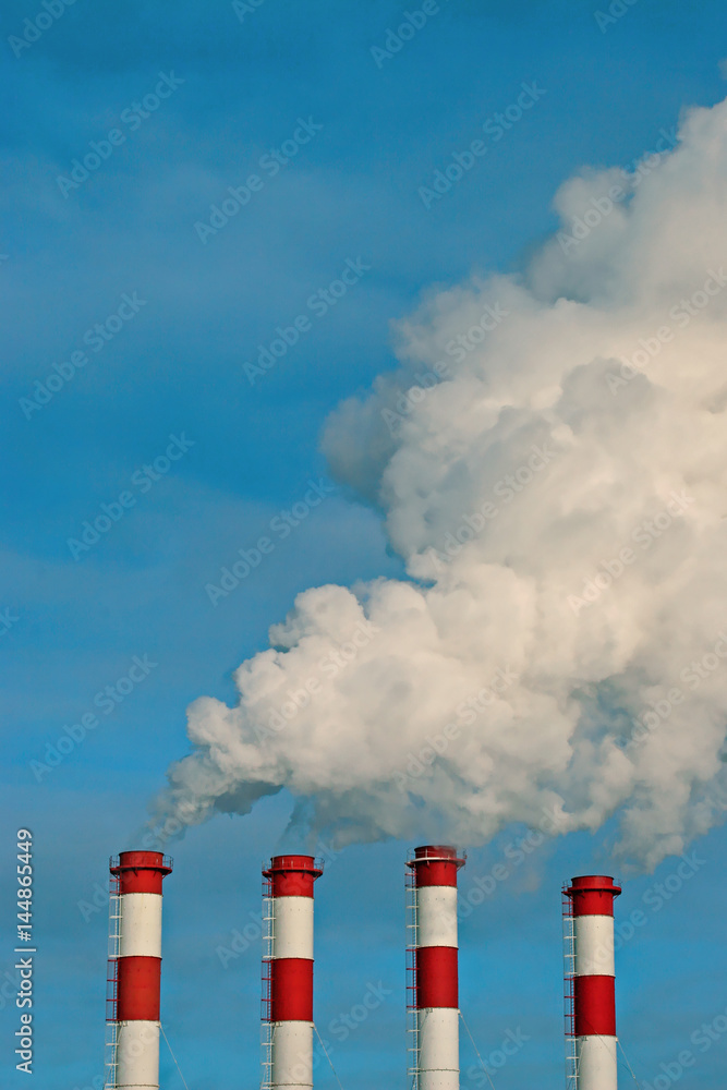 Blue sky and four smokestacks of a thermal power station with clouds of smoke, air steam. Vertical image. Blue sky and four smokestacks of a thermal power station with clouds of smoke, air steam. Vertical image.