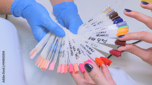 Nail technician shows the color palette of nail services in beauty salon. Woman selects of nail design.