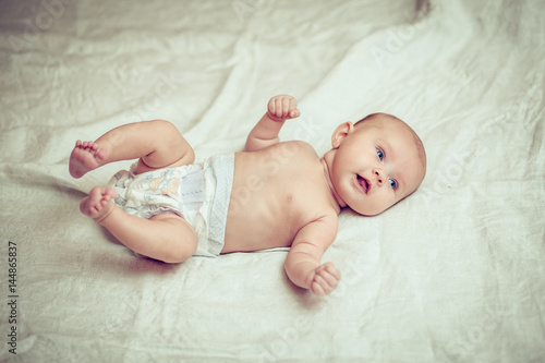 happy baby lying on white sheet and holding his legs © honcharr