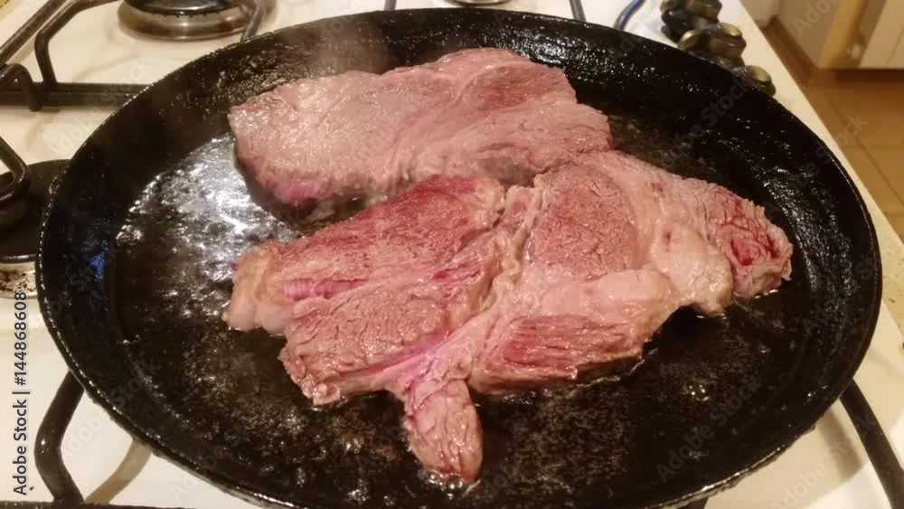 Two fat juicy steaks from marbled beef are fried in oil in a frying pan Two fat juicy steaks from marbled beef are fried in oil in a frying pan