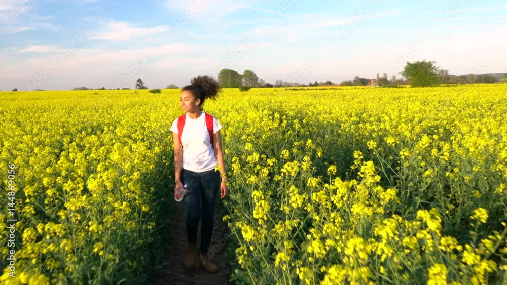 4K video clip of beautiful happy mixed race African American girl teenager female young woman hiking with red backpack and bottle of water in field of rape seed yellow flowers 4K video clip of beautiful happy mixed race African American girl teenager female young woman hiking with red backpack and bottle of water in field of rape seed yellow flowers