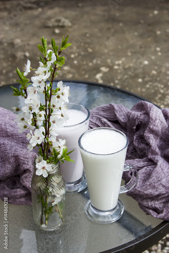 Bild auf Leinwand Milk cocktail in two tall glasses on a table next to a vase with white spring fl