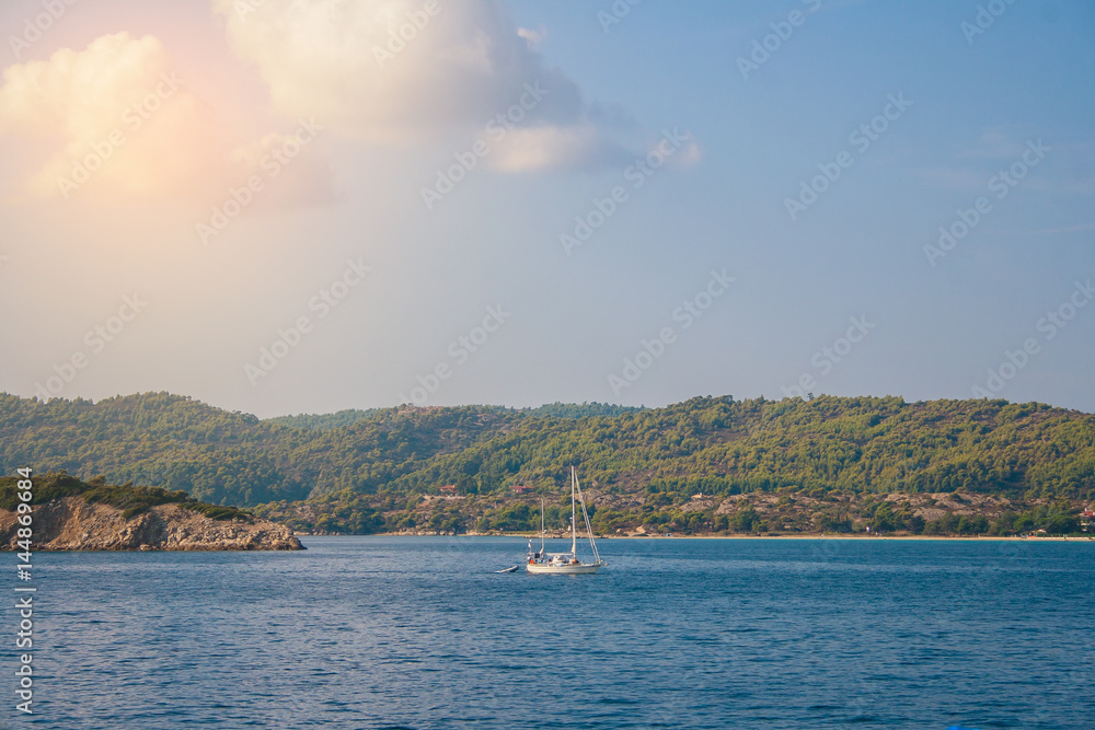 Sailing boat sailing on the sea at the backdrop of green mountains. Landscapes of the Halkidiki Peninsula in Greece