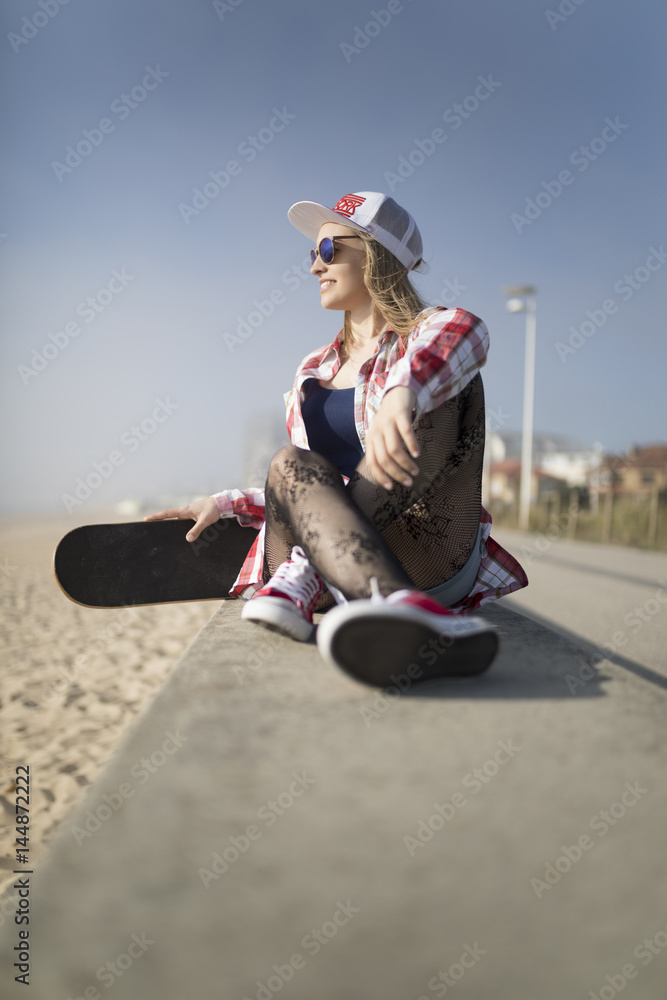 Happy smiling fashion young woman posing with a skateboard