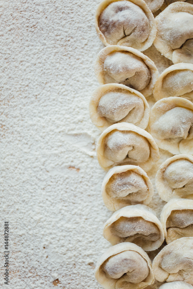 Even rows of freshly made meat pockets lying on surface covered with flour.