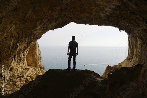 Hiker pauses to watch the sea from a cave, Grotta dei Falsari,  Noli, Liguria, Italy