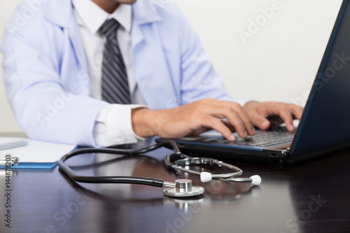 stethoscope is lying on the table near male doctor typing on laptop computer