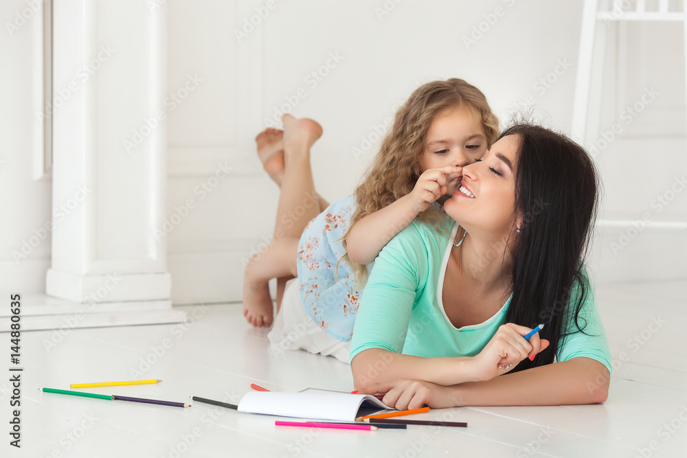 Little cute daughter and her mother drawing with colorful pencils and having fun together. Pretty child and mom playing indoors. Happy family spending time by drawing. Little cute daughter and her mother drawing with colorful pencils and having fun together. Pretty child and mom playing indoors. Happy family spending time by drawing.