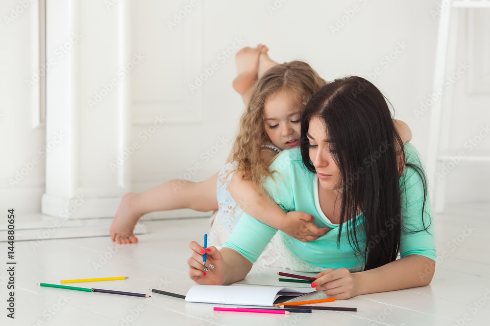 Little cute daughter and her mother drawing with colorful pencils and having fun together. Pretty child and mom playing indoors. Happy family spending time by drawing. Little cute daughter and her mother drawing with colorful pencils and having fun together. Pretty child and mom playing indoors. Happy family spending time by drawing.