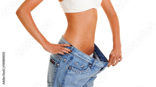Woman shows her weight loss by wearing an old jeans, isolated on white background. Close up of sporty and beautiful female body. Healthy lifestyle, dieting, fitness, weight loss concept
