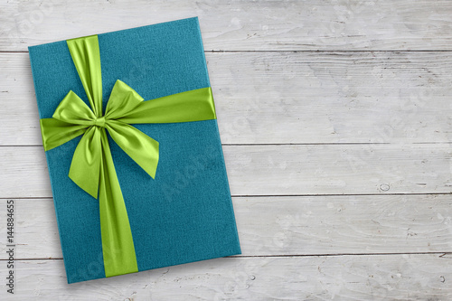 Blue gift box with green ribbon over light wood, top view from above photo