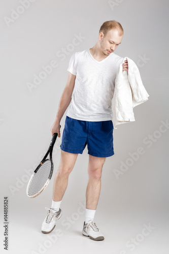 young tennis player with towel holding tennis racket after training on gray background