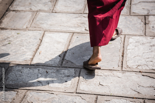 Feet ot a buddhist monk wearing sandals and traditional red robe walking in the midday sun with a strongly defined shadow. Kopan monastery, Kathmandu, Nepal. photo