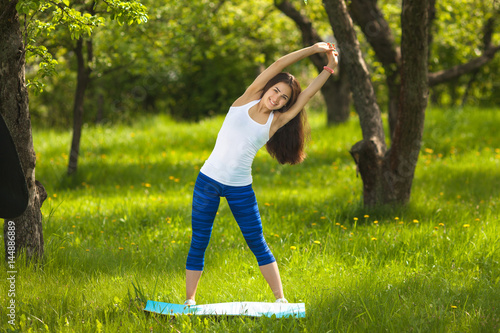 Young girl working out outdoors. Beautiful woman doing pilates, yoga and fitness exercices on nature. photo