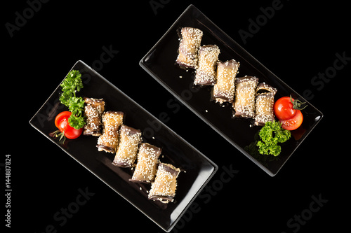 Eggplant rolls with cheese, garlic and sesame on black plates with herbs and tomato. Top view and isolated on black
