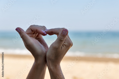 Female hands folded in shape of heart against sea shore