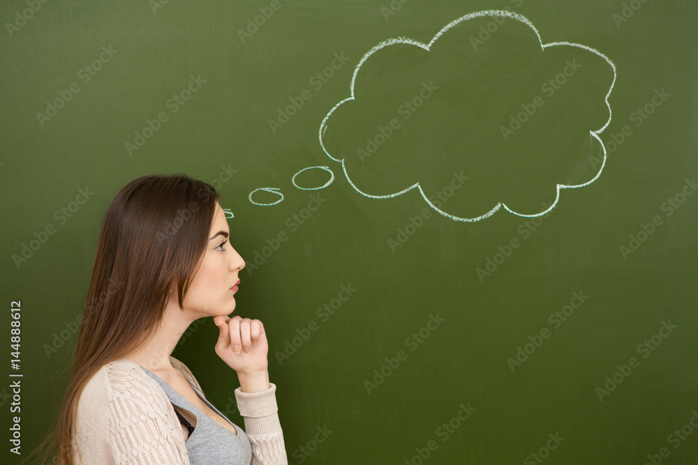 Young woman thinking with a blank thought bubble drawn on a chalkboard behind her