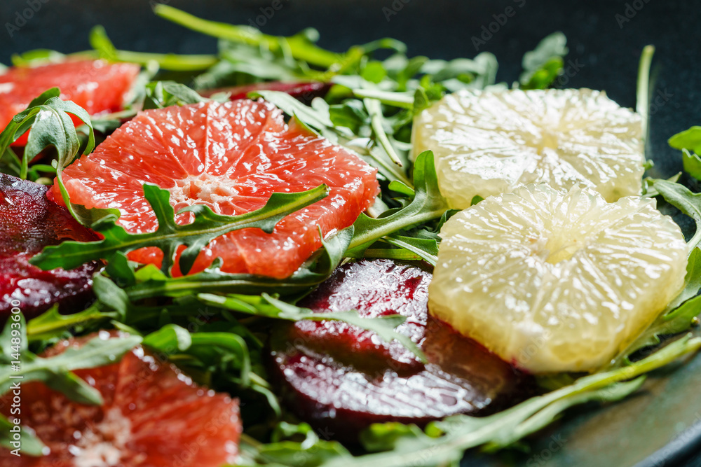 Fresh mix salad of red beet, grapefruit and orange on a cushion of arugula in a black dish. Closeup view.