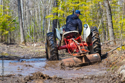 Man on a vintage tractor grading a muddy road.