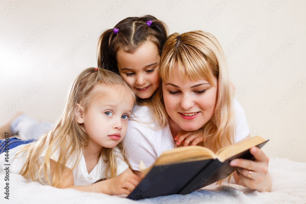 happy loving family. pretty young mother reading a book to her daughters Mom and two little girls book