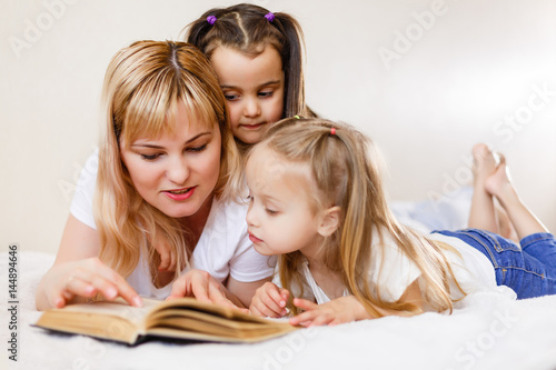 happy loving family. pretty young mother reading a book to her daughters Mom and two little girls book