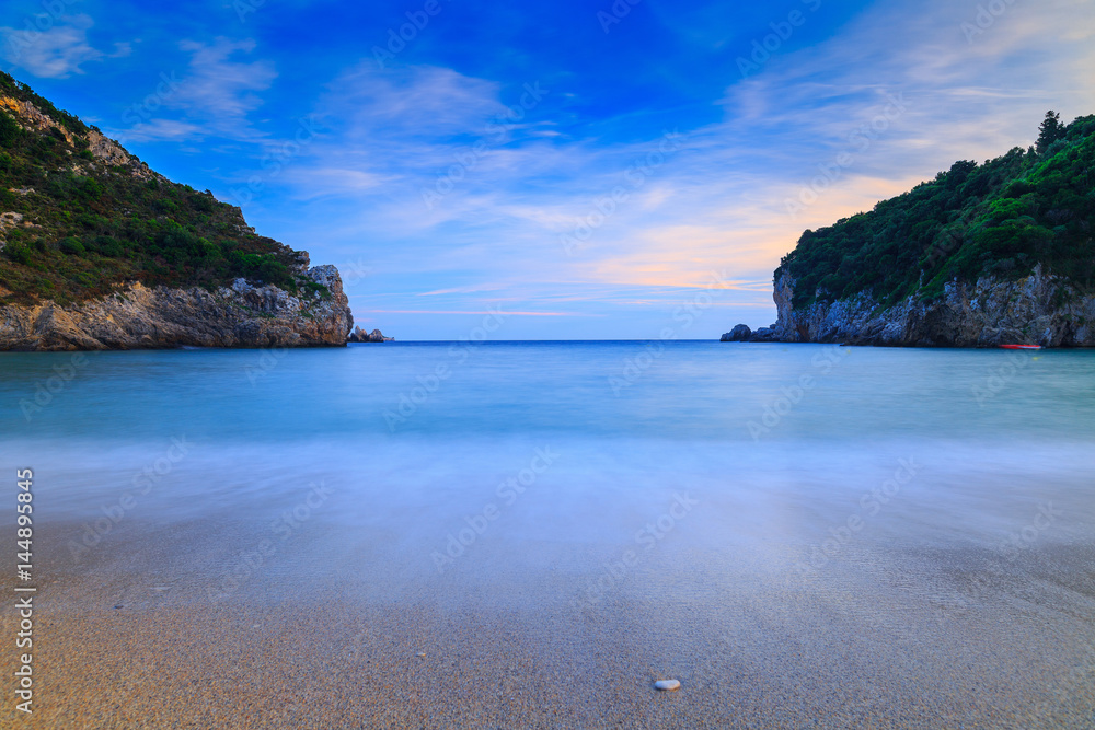 Obraz premium Long exposure landscape of Paleokastritsa famous sand beach in close bay on Corfu island at dusk, Ionian archipelago, Greece.