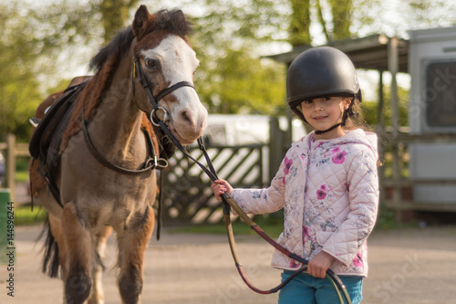 Obraz na plátně Young girl wearing riding helmet leading Welsh pony