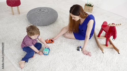 Young mother playing with her small son with the cars on the carpet slow motion photo