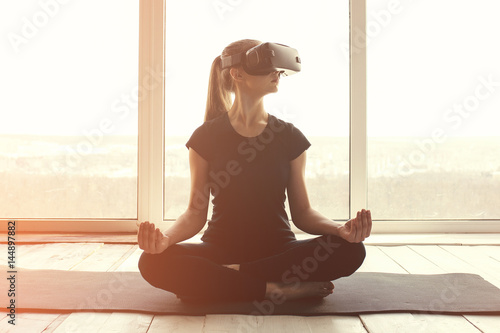 A young beautiful girl in virtual reality glasses makes yoga and aerobics remotely. Future technology concept. Modern imaging technology. Classes in single sports remotely.