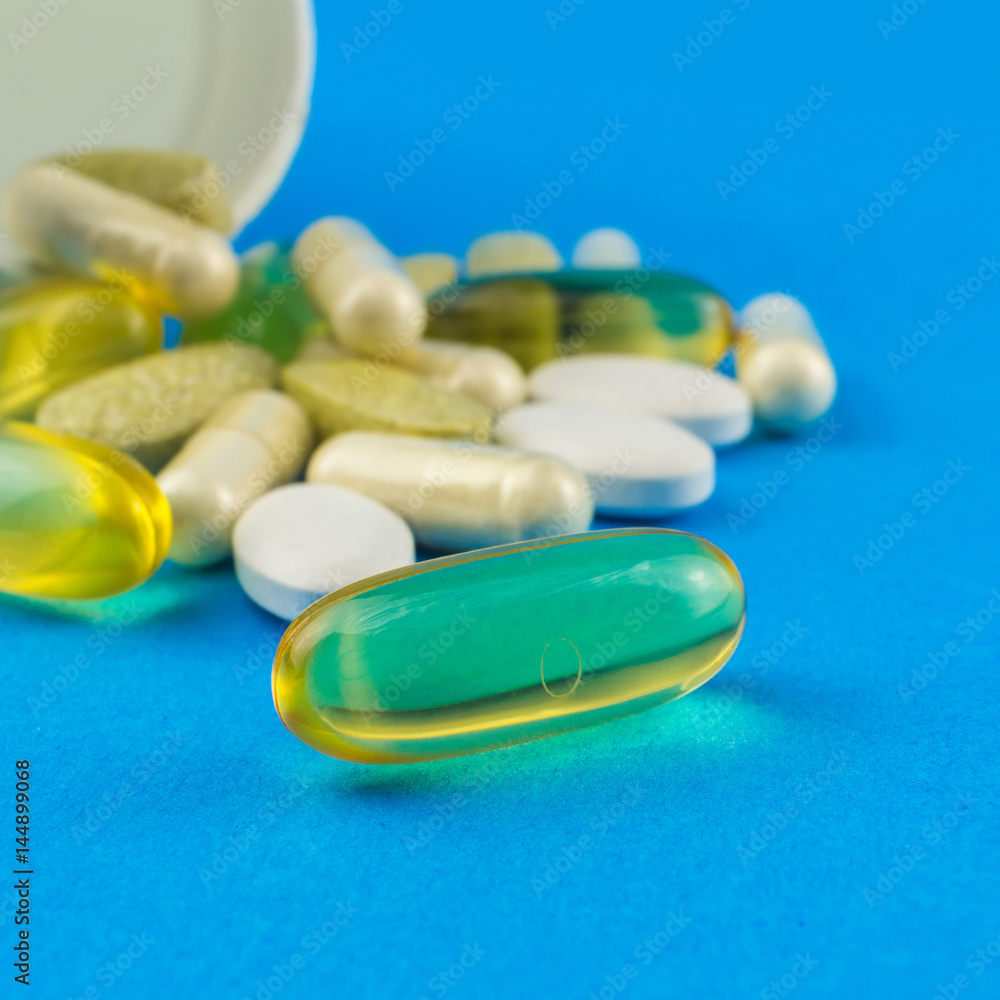 Supplement of omega-3 capsule on foreground in the focus, vitamin complex, glucosamine capsules and white container on blue background Supplement of omega-3 capsule on foreground in the focus, vitamin complex, glucosamine capsules and white container on blue background