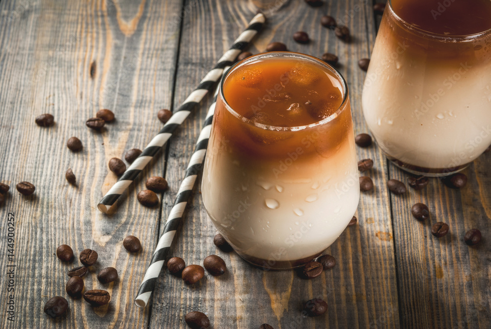 Cold coffee with milk, caramel and ice, with cubes of frozen coffee. Cappuccino, frapuchchino or latte. On awooden dark table, with coffee beans and striped straws. Copy space Cold coffee with milk, caramel and ice, with cubes of frozen coffee. Cappuccino, frapuchchino or latte. On awooden dark table, with coffee beans and striped straws. Copy space