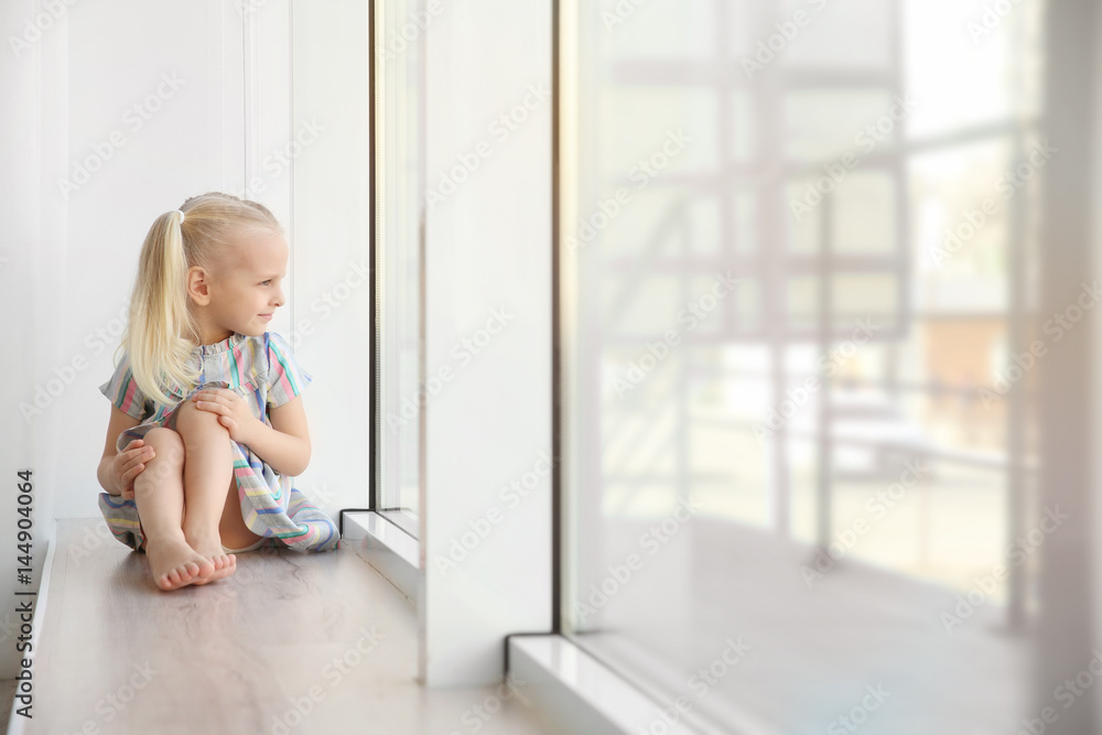 Cute little girl sitting on windowsill Cute little girl sitting on windowsill