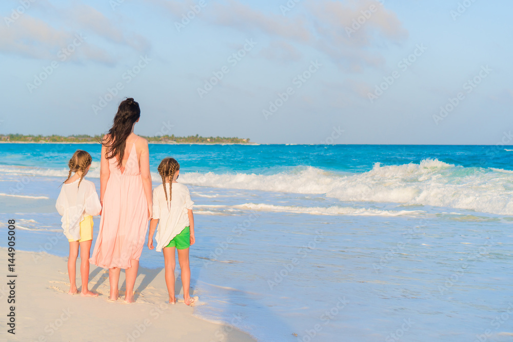 Adorable little girls and young mother on white beach on sunset