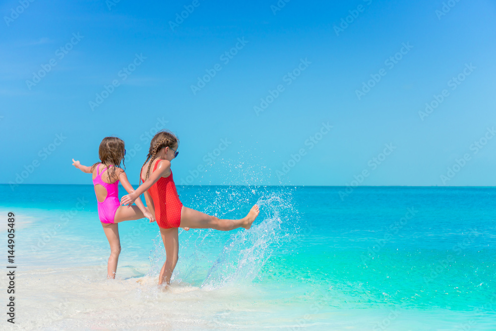 Little girls having fun at tropical beach playing together at shallow water