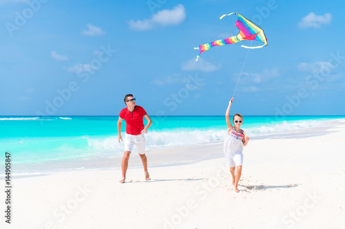 Happy father and cute little daughter flying kite together at tropical beach
