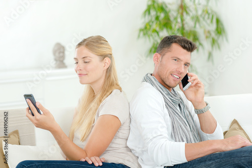 Man and lady on couch, each using their own cellphone