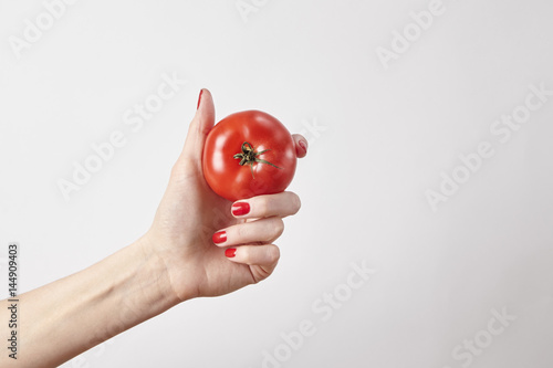 Fresh vegetable tomato in woman hand, fingers with red nails manicure, isolated on white background, healthy lifestyle concept