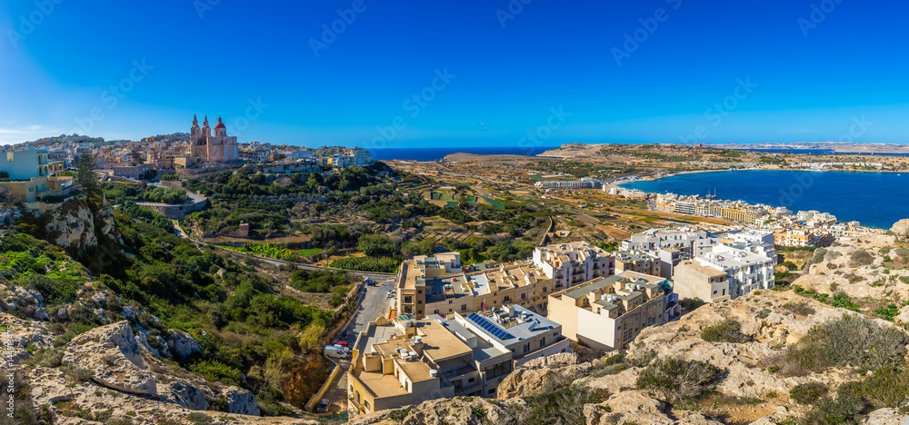 Naklejka premium Il-Mellieha, Malta - Beautiful panoramic skyline view of Mellieha town on a bright summer day with Paris Church, Agatha Red Tower and Mellieha beach at background with blue sky and clouds