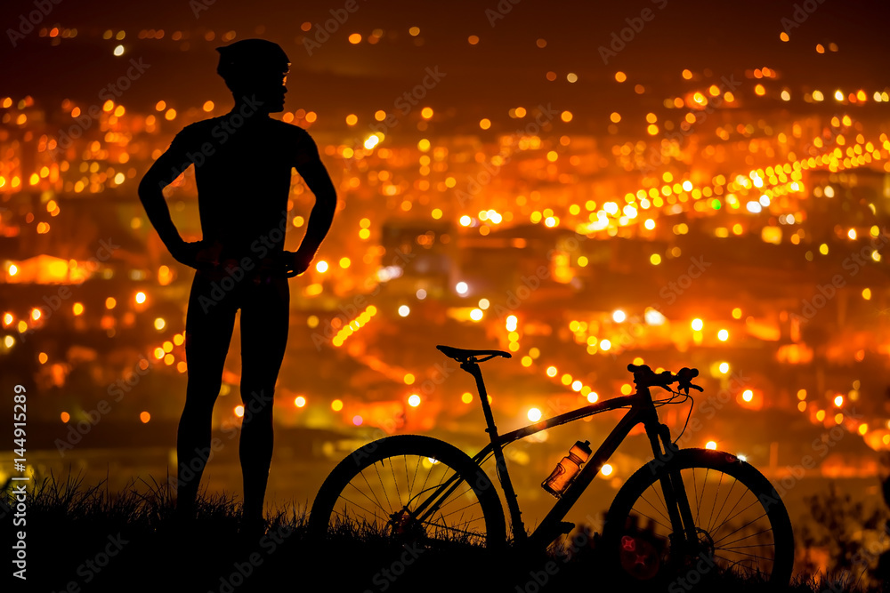 Obraz premium athlete is standing with bicycle, resting with the night city view