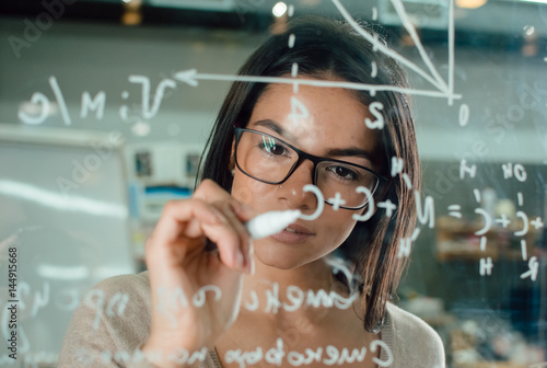 Young attractive female office worker writing on glass whiteboard