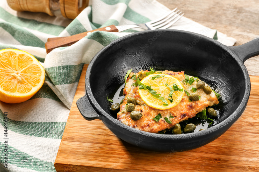 Frying pan with delicious chicken piccata on wooden board Frying pan with delicious chicken piccata on wooden board