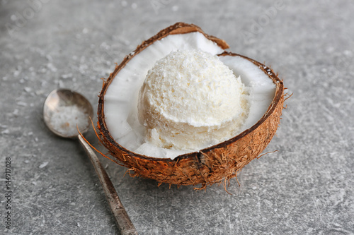 Fresh ball of ice cream in half of coconut and spoon on grey background
