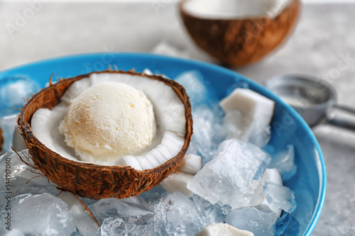 Half of coconut with fresh ice cream ball cooling on icy cubes in blue bowl
