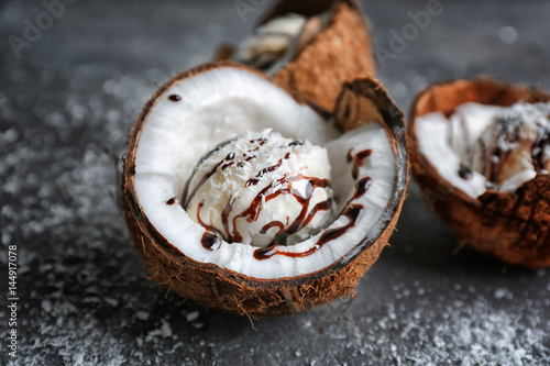 Ice cream with desiccated coconut and chocolate syrup in half of nut on grunge background
